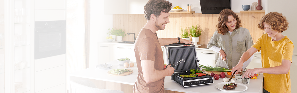 Tata z dziećmi szykuje jedzenie na grillu elektrycznym