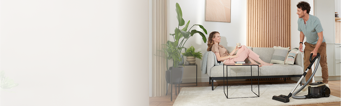 Mężczyzna odkurza dywan, kobieta siedzi na kanapie