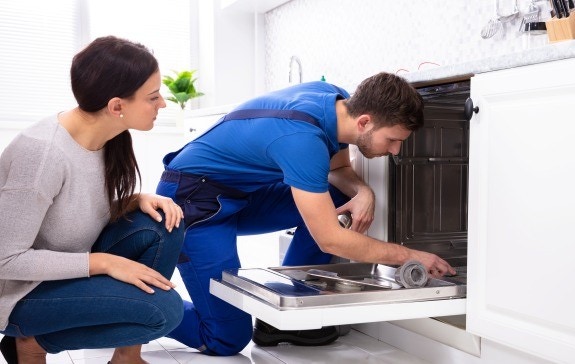 Serwisant naprawia zmywarkę, kobieta kuca obok niego