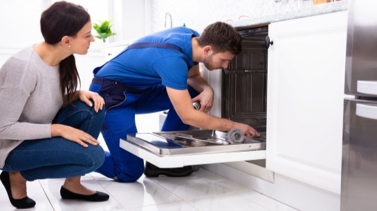 Serwisant naprawia zmywarkę, kobieta kuca obok niego