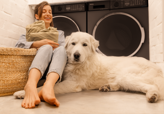 Kobieta i duży biały pies siedzą na podłodze, w tle czarna suszarka i pralka 