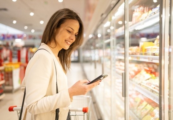 Kobieta w markecie korzysta z telefonu kom&oacute;rkowego