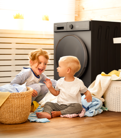 dziewczynka i chłopiec siedzą przy suszarce, na podłodze leżą ubrania