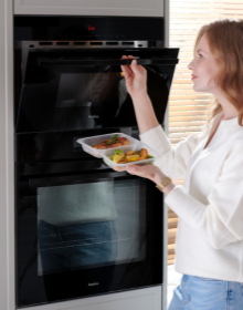 kobieta wkłada jedzenie do kuchenki mikrofalowej