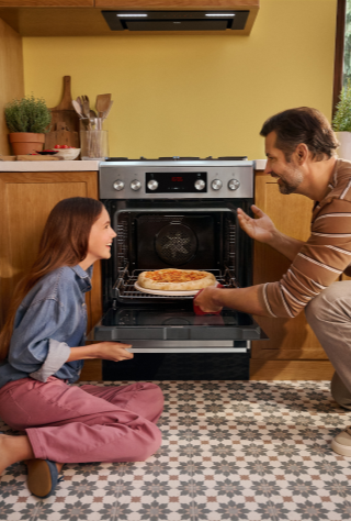 Tata z c&oacute;rką wyjmują pizzę z kuchni wolnostojącej