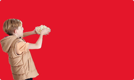 chłopiec z miską popcornu w rękach na czerwonym tle