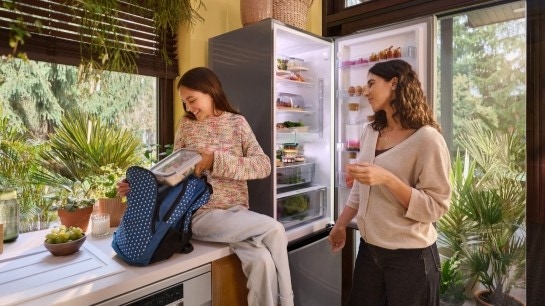 mama z c&oacute;rką stoją przy otwartej lod&oacute;wce, c&oacute;rka pakuje plecak