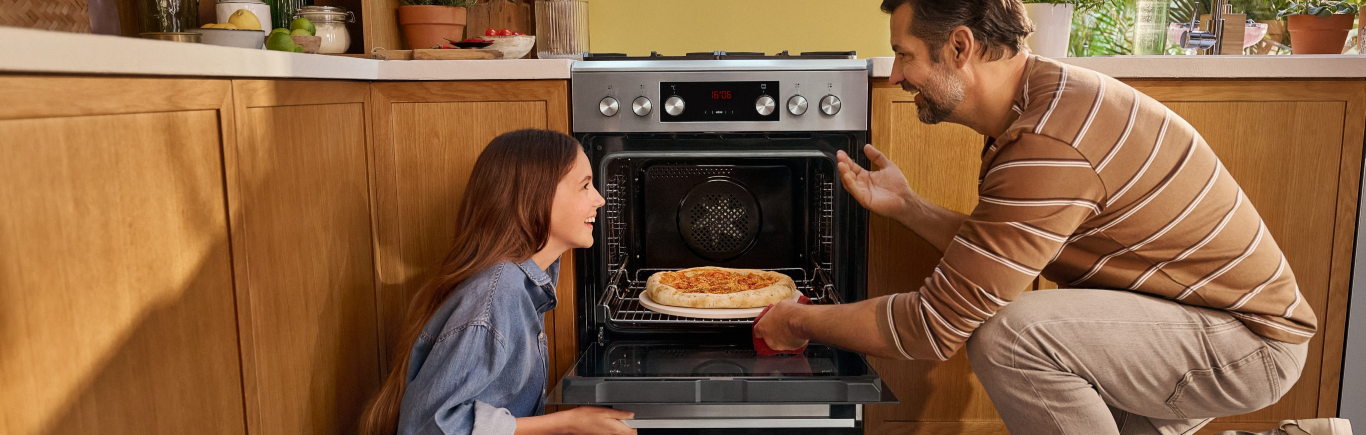 Tata z c&oacute;rką wyjmują pizzę z kuchni wolnostojącej