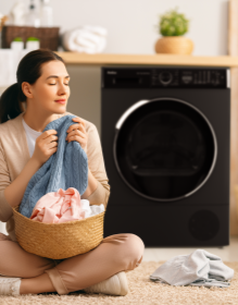 kobieta z praniem siedzi na podłodze, w tle czarna suszarka